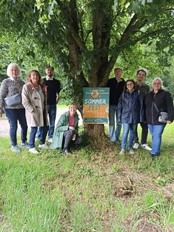 Zu sehen sind verschiedene grüne Mitglieder zusammen mit dem Plakat zum Sommerfest vor einem Baum im Kleintierzüchterareal in Schwieberdingen