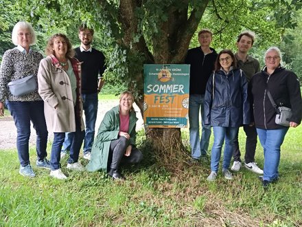 Zu sehen sind verschiedene grüne Mitglieder zusammen mit dem Plakat zum Sommerfest vor einem Baum im Kleintierzüchterareal in Schwieberdingen