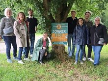 Zu sehen sind verschiedene grüne Mitglieder zusammen mit dem Plakat zum Sommerfest vor einem Baum im Kleintierzüchterareal in Schwieberdingen